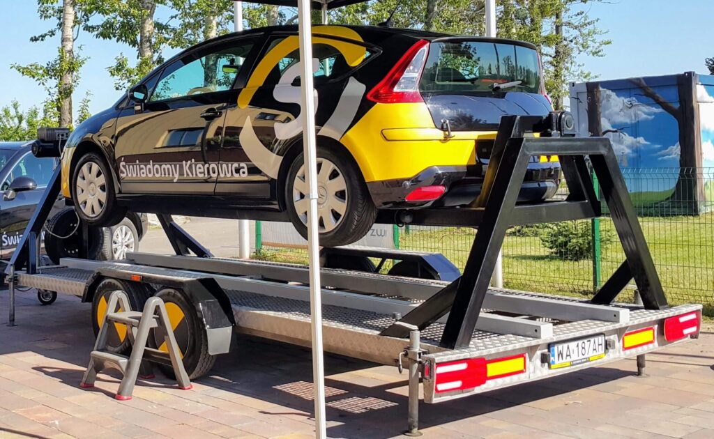Na zdjęciu widoczny jest symulator dachowania wykorzystywany podczas szkoleń z defensywnej jazdy. Umożliwia on praktyczne ćwiczenie zachowania kierowcy w przypadku przewrócenia pojazdu oraz uczy prawidłowego opuszczania samochodu po wypadku, zwiększając świadomość i bezpieczeństwo uczestników ruchu drogowego.