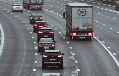 Na zdjęciu widać duży ruch na wielopasmowej drodze, z samochodami osobowymi oraz ciężarówkami poruszającymi się w kilku pasach. Pojazdy zachowują niewielkie odstępy, a część z nich ma włączone światła hamowania. Zdjęcie dobrze ilustruje jazdę w intensywnym ruchu, konieczność zachowania odpowiedniego odstępu oraz przewidywania zachowania innych kierowców.